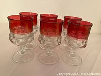 Set of six cranberry and clear patterned water goblets arranged in a cluster on a light surface.