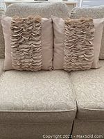 Two neutral beige decorative cushions on patterned sofa, showcasing frill fabric accent detail