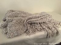 Photo of a folded greige colored popcorn stitch throw blanket with fringed edges lying on a flat surface.