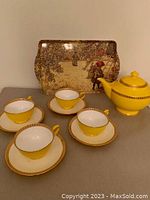Photo shows the yellow ceramic teapot, four yellow cups on saucers with gold rims, and the melamine tray with apple harvest design in background.