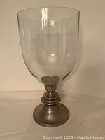 Photo shows a large glass candle holder with a clear glass bowl and a metal base. The candle holder stands approximately 18 inches tall. The base has a tiered metal design and the glass is smooth and round.