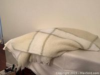 Folded light beige mohair throw blanket draped on a surface, showing soft texture and some fringe ends.