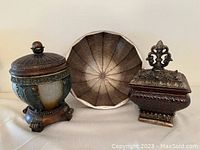 Three decorative items: ornate round footed bowl with lid, wooden bowl with ribbed interior, ornate square box with lid featuring detailed finial.