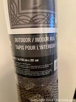 Photo showing the label of a wrapped outdoor/indoor rug indicating dimensions and material composition.