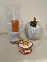 Porcelain pumpkin, glass hurricane candle holder with orange candle, and round decorative box with fall colors