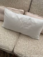 Plain rectangular throw pillow in neutral tone with button styling, measured approximately 22x9 inches, placed on a patterned beige couch.