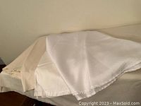 Stack of four round tablecloths, one white and three cream, folded and laid on a surface.