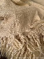 Close-up of the cream-colored throw showing the variable thickness yarn and long twisted fringes at the edge.