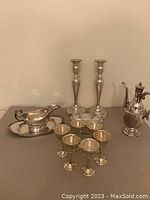 Photo showing silver plate gravy boat on tray, six small silver plate sherry glasses, a pair of tall silver plate candlesticks, and a small silver plate teapot.