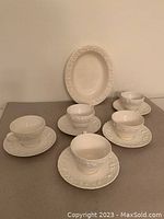 Five white embossed Wedgwood cups and saucers displayed surrounding a white embossed serving platter.