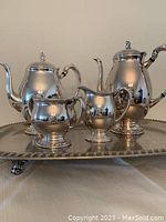 Front view of the entire tea service including coffee pot, teapot, sugar bowl, cream pitcher on the footed tray.