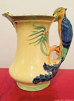 Side view of the yellow ceramic water pitcher featuring a detailed parrot-shaped handle and hand-painted greenery.