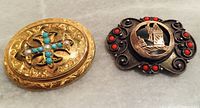 Two antique brooches side by side on a flat surface showing gold-tone piece with turquoise and pearl, and silver-tone piece with red coral and cut-out figure