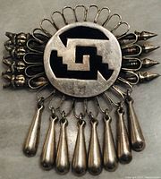 Front view of the Navajo silver brooch showing central circular element with black geometric pattern, silver loops around the edge, arrowhead shaped accents on sides, and seven hanging silver teardrop dangles.