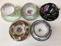 Top-down view of five bone china teacup and saucer sets arranged in two rows showing floral designs and colors.