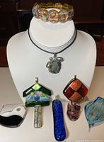 Display of stretch bracelet with round Murano glass beads, plastic cord chain necklace with multicolor pendant, and seven assorted Murano glass pendants.