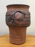 Front side of the Jack Herman signed stoneware vase showing the textured circular design and reddish-brown matte finish.