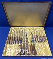Open original box displaying all 16 utensils on gold satin lining