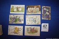 Seven postcards showing classic Easter motifs including children, rabbits, eggs, flowers, and embossed designs on a blue background.