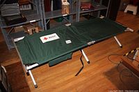 Full view of the open folding aluminum cot, showing green canvas fabric and structure on wooden floor.