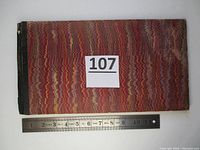 Closed view of the booklet showing marbled cover pattern and size comparison with a ruler.