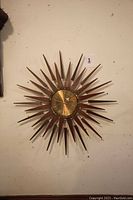 Full front view of the sunburst clock showing teak wood spokes and brass center