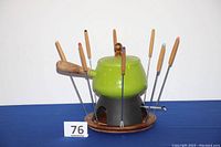 Full assembled fondue set with pot, stand, base, 8 forks, and lid shown from side angle.