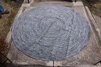 Full view of round blue braided rug laying flat on outdoor concrete surface, showing overall size and shape.