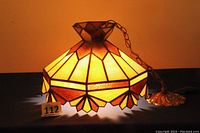 Lamp shade lit up to show stained glass colors and geometric pattern. Includes hanging chain and decorative ceiling mount.