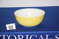 Side view of yellow Pyrex mixing bowl showing exterior and partial interior, set on blue fabric background with lot number 69.