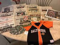 Table display of assorted original Cal Ripken Streak newspapers, Baltimore Orioles jersey, camouflage hat, medallions, newspaper clippings, and collectible cards.