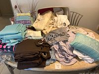 Overall assortment of bed linens, curtains, blankets, and pillows displayed on a table showing variety of fabric colors and types.