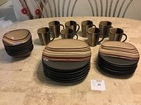 Image shows complete 8 place dinnerware set stacked: mugs in the back, then bowls, dinner plates, and salad plates in front.