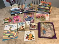 Photo showing multiple stacks of assorted children's books including Dr. Seuss, Disney Princess, Barbie and other titles spread on table.