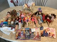 Table with 26 dolls, 2 horses, 5 books, and doll clothing laid out for display.