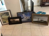 Four framed art pieces grouped together showing variety of themes and sizes on tile floor
