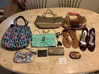 Full lot arranged on table showing five handbags, wallets, two pairs of shoes, and accessory.
