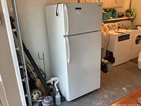 White Kelvinator refrigerator freezer beside wall and other laundry room appliances