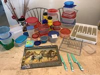 Overview of kitchen items on counter, assortment of containers, knives, racks, cutlery tray, and cutting board