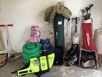 Wide view of sporting goods including golf bag with clubs, black ski boots, sleeping bags, Razor scooter, dog swim vest, and thermos.