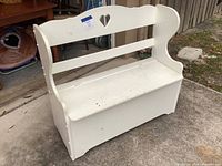 Front view of white painted solid wood storage bench with heart cut-out on backrest, showing overall condition and wear.
