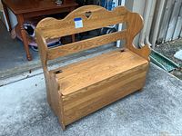 Front view of wooden storage bench/toy box with heart cutout on backrest, showing hinges on top panel and natural wood grain.
