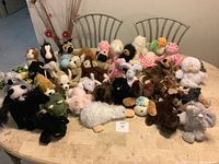 Wide view of 34 assorted Webkinz plush toys arranged on a dining table showing variety of animals and colors