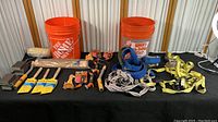 Wide view of paint brushes, sanding blocks, straps, and buckets on a table
