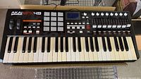 Front view of AKAI MPK49 controller showing 49 keys, pitch and modulation wheels, 12 pads, and buttons.