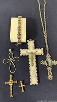 Full lot showing five cross pendants, one cross necklace, and one gemstone bracelet on dark fabric background.