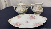 Three-piece set of Haviland Limoges porcelain dishes with pink floral poppy design and gilded trim on black cloth background.