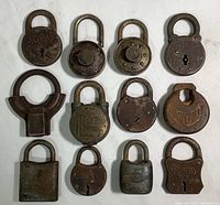 All 12 vintage padlocks arranged on a flat surface showing fronts including brand names and various shapes.