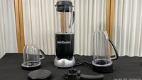 NutriBullet RX NB301 blender base with three clear plastic blender cups with handles arranged around it.