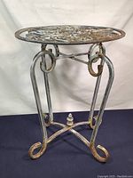 Full view of the metal plant stand showing the oval top and curved legs with decorative scrolls.